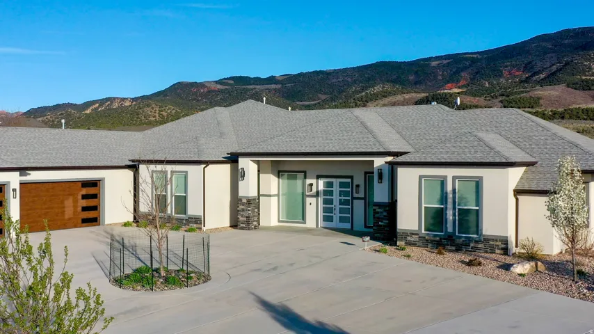 Contemporary stucco exterior with stone accents, a wood-finish garage door, and a light gray shingle roof