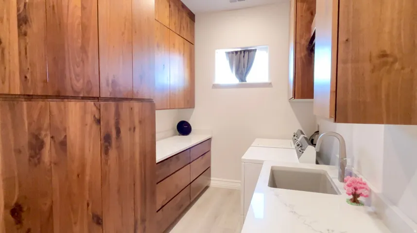 Laundry room featuring extensive wood cabinetry, white quartz countertops, a utility sink with a high-arc faucet, and light wood-finish flooring