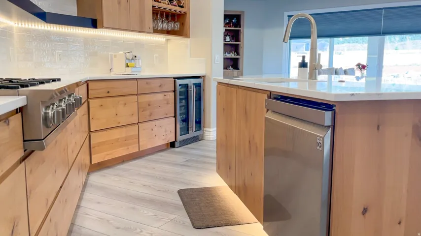 Kitchen featuring light wood-finish cabinetry, white countertops, a built-in beverage cooler, stainless steel appliances, and wood-finish flooring