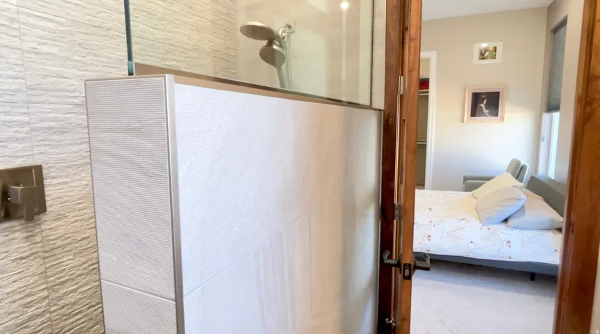 Tiled shower enclosure featuring a glass partition, rainfall showerhead, and a wall-mounted shower control