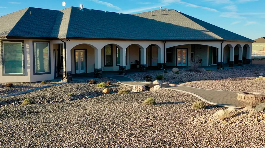 Expansive rear exterior featuring a covered patio with arched openings, multiple large windows, and a gravel landscape