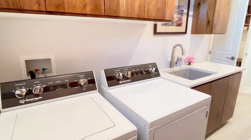 Laundry area featuring wood-finish cabinetry, a utility sink with a gooseneck faucet, light-toned countertop, and light-colored flooring
