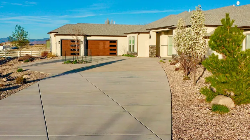 Extensive paved driveway leads to a stucco exterior property featuring a two-car garage with modern wood-finish doors and frosted glass inserts