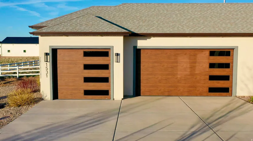 Exterior featuring two modern wood-finish garage doors with horizontal window inserts, stucco siding, a concrete driveway, and exterior lighting fixtures
