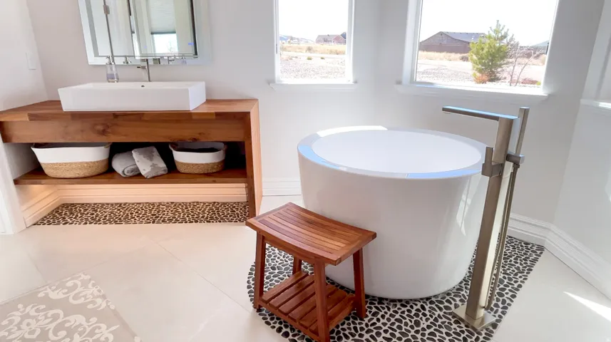 Modern freestanding soaking tub with a brushed nickel floor-mounted faucet, set on black river rock tile