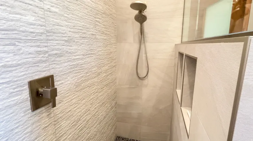 Shower featuring textured wall tile, integrated niche shelving, a handheld showerhead, and a bronze-finish shower valve