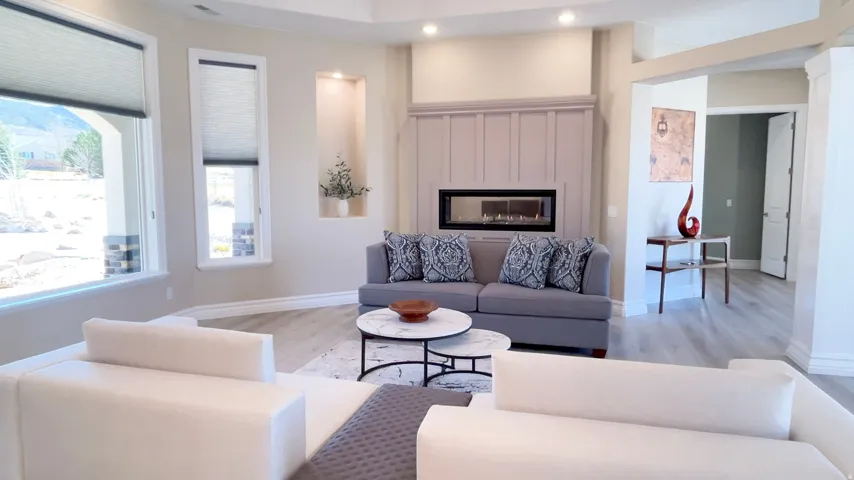Living area featuring a linear gas fireplace with a light-toned board and batten surround, recessed lighting, large windows with cellular shades, built-in wall niches, and wood-finish flooring