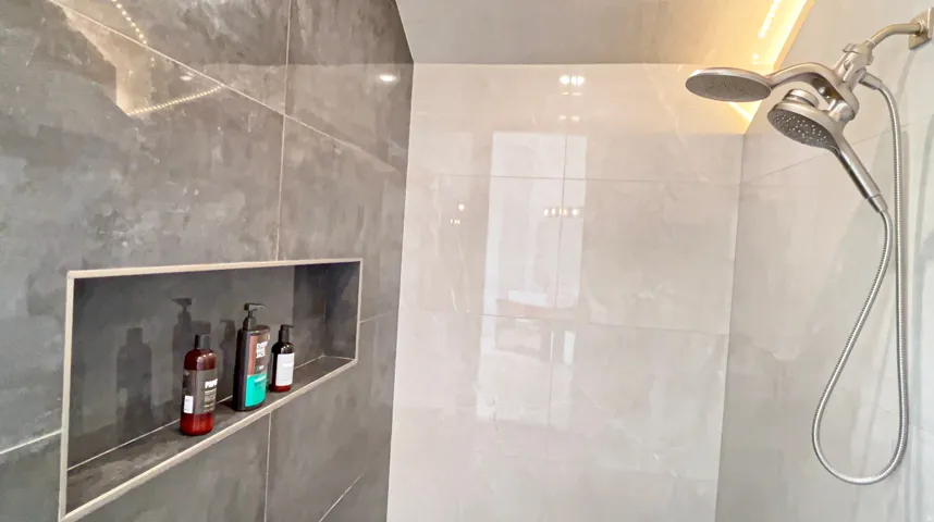 Shower enclosure featuring large format light gray wall tiles and a recessed niche within the dark gray tiled wall