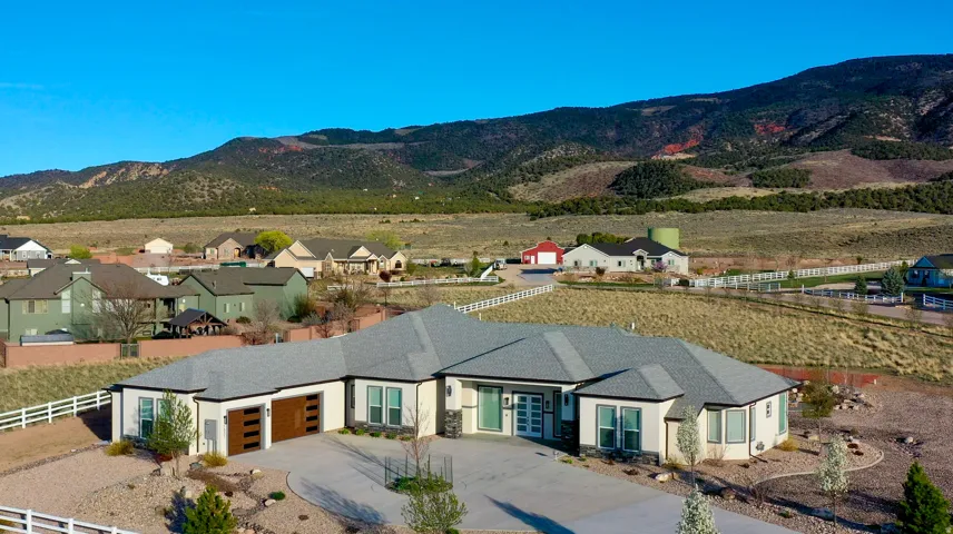 Modern ranch-style residence featuring a multi-gabled roofline, light-colored stucco exterior, and a prominent mountain backdrop