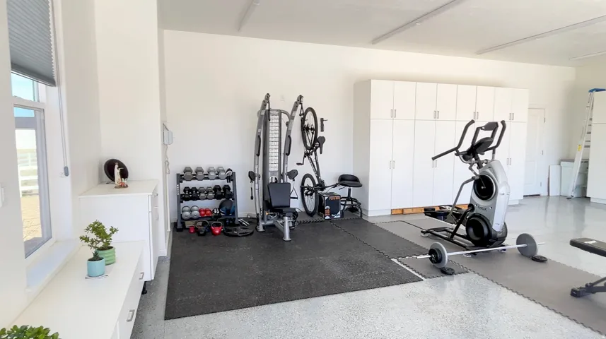 Spacious garage featuring ample white cabinetry, durable epoxy flooring, and a large window providing natural light