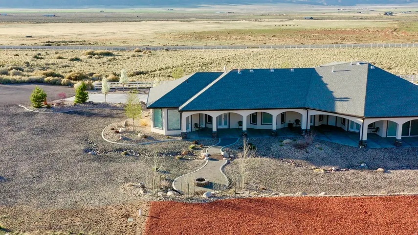 Expansive single-story residence featuring a large covered patio with multiple arched openings, a dark shingle roof, and a stone-lined pathway