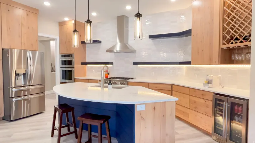 Contemporary kitchen featuring a curved island with a white countertop and blue paneling, light wood-finish cabinetry, stainless steel appliances, a built-in wine rack, and a beverage cooler