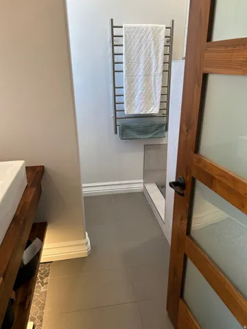 Bathroom featuring large format floor tiles, a built-in towel warmer, and a wood-frame door with frosted glass panels
