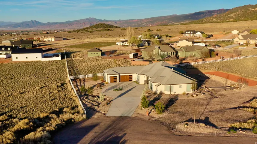 Modern ranch-style residence featuring a light-toned exterior, a multi-car garage with wood-finish doors, and a paved driveway