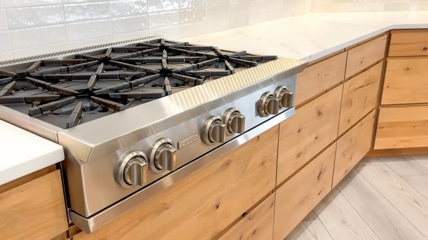 Stainless steel range top with professional-grade grates, integrated into light wood-finish cabinetry