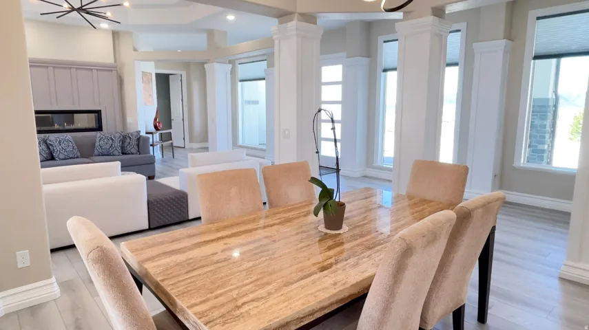 Open-concept interior featuring light wood-finish flooring, a linear fireplace with a paneled surround, recessed lighting, and decorative columns