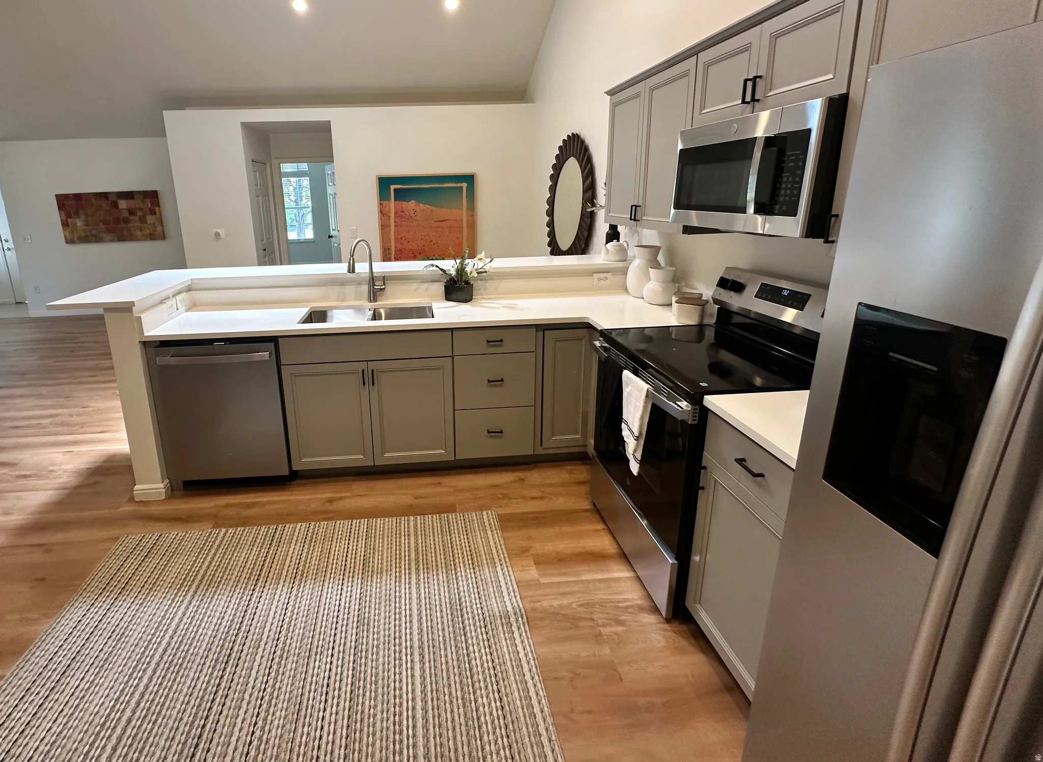 Modern kitchen featuring light wood-finish flooring, white countertops, gray cabinetry, and stainless steel appliances including a refrigerator, range, microwave, and dishwasher