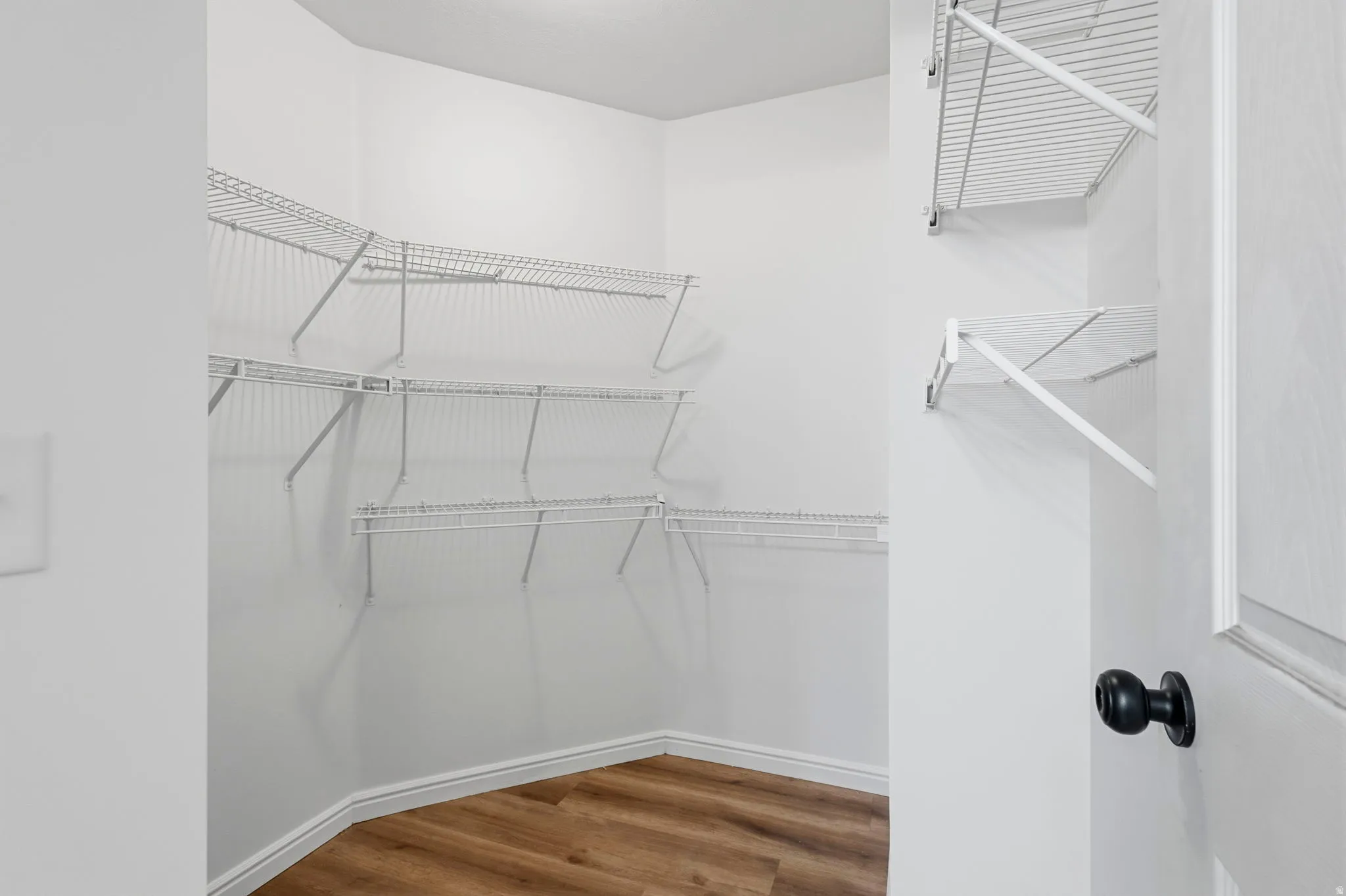 Walk-in closet featuring wire shelving, white walls, and wood-finish flooring