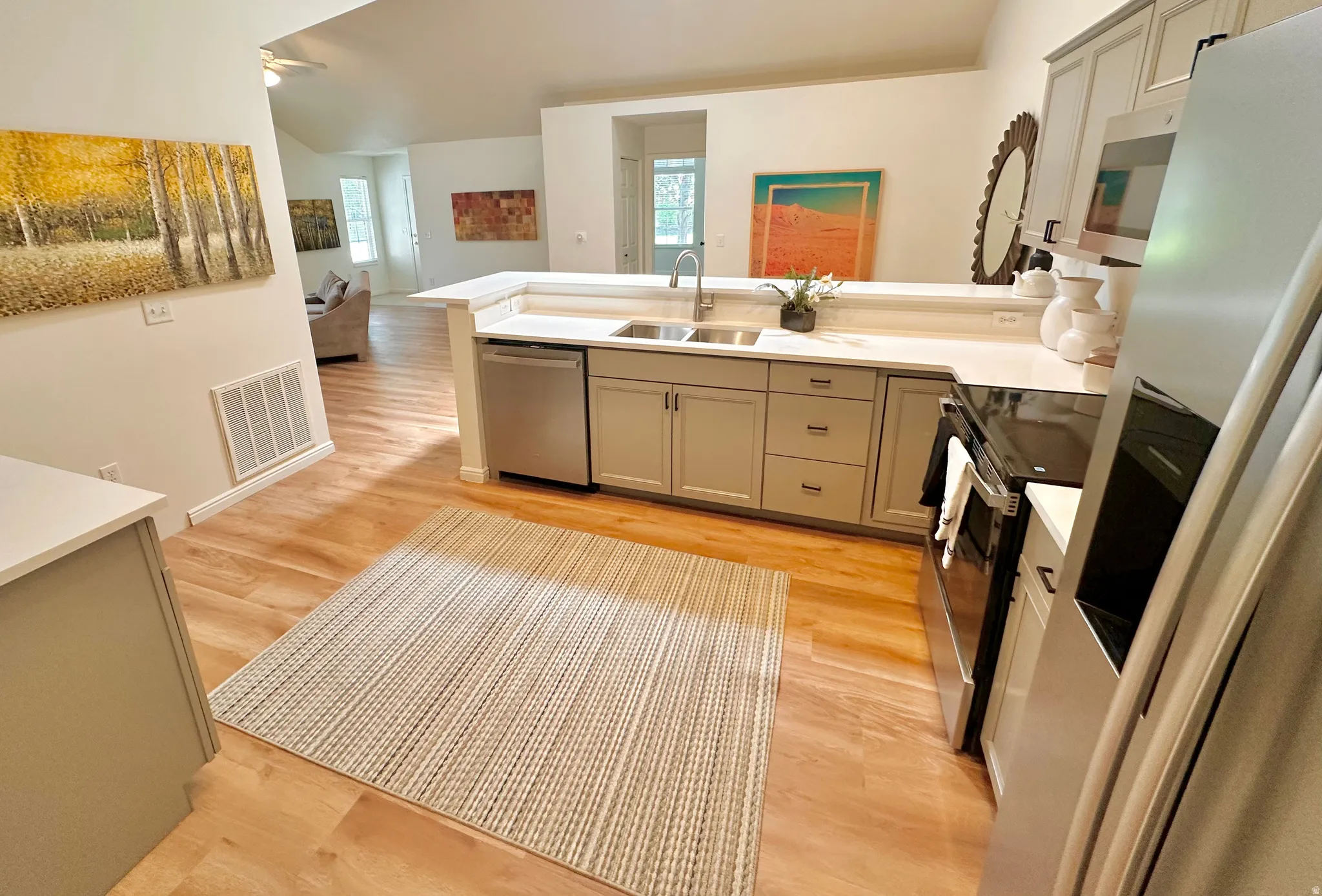 Modern kitchen featuring light gray cabinetry with dark hardware, a stainless steel sink with a gooseneck faucet, light-toned countertops, and wood-finish flooring