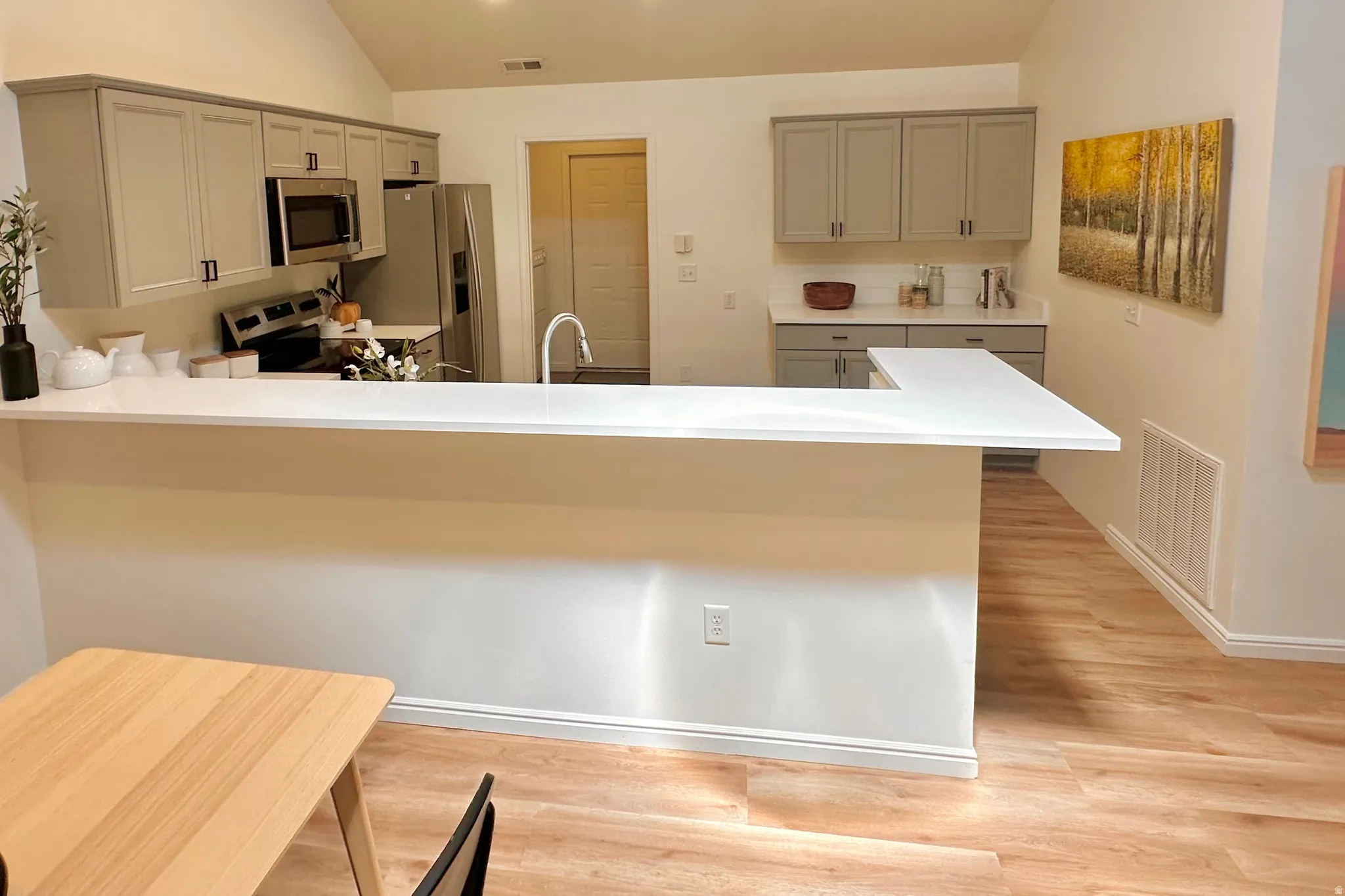 Kitchen featuring a peninsula breakfast bar, wood-finish flooring, vaulted ceilings, grey shaker-style cabinetry, and stainless steel appliances
