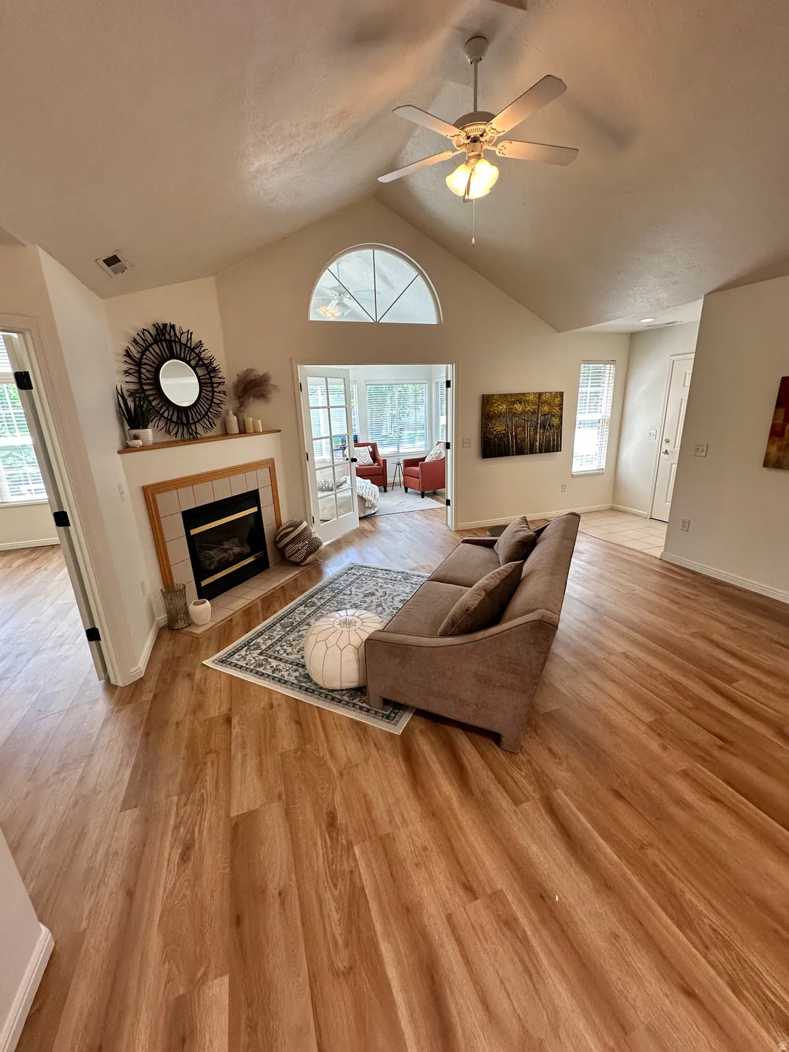 Bright living area featuring wood-finish flooring, a vaulted ceiling, and a fireplace with a tile surround and wood mantel