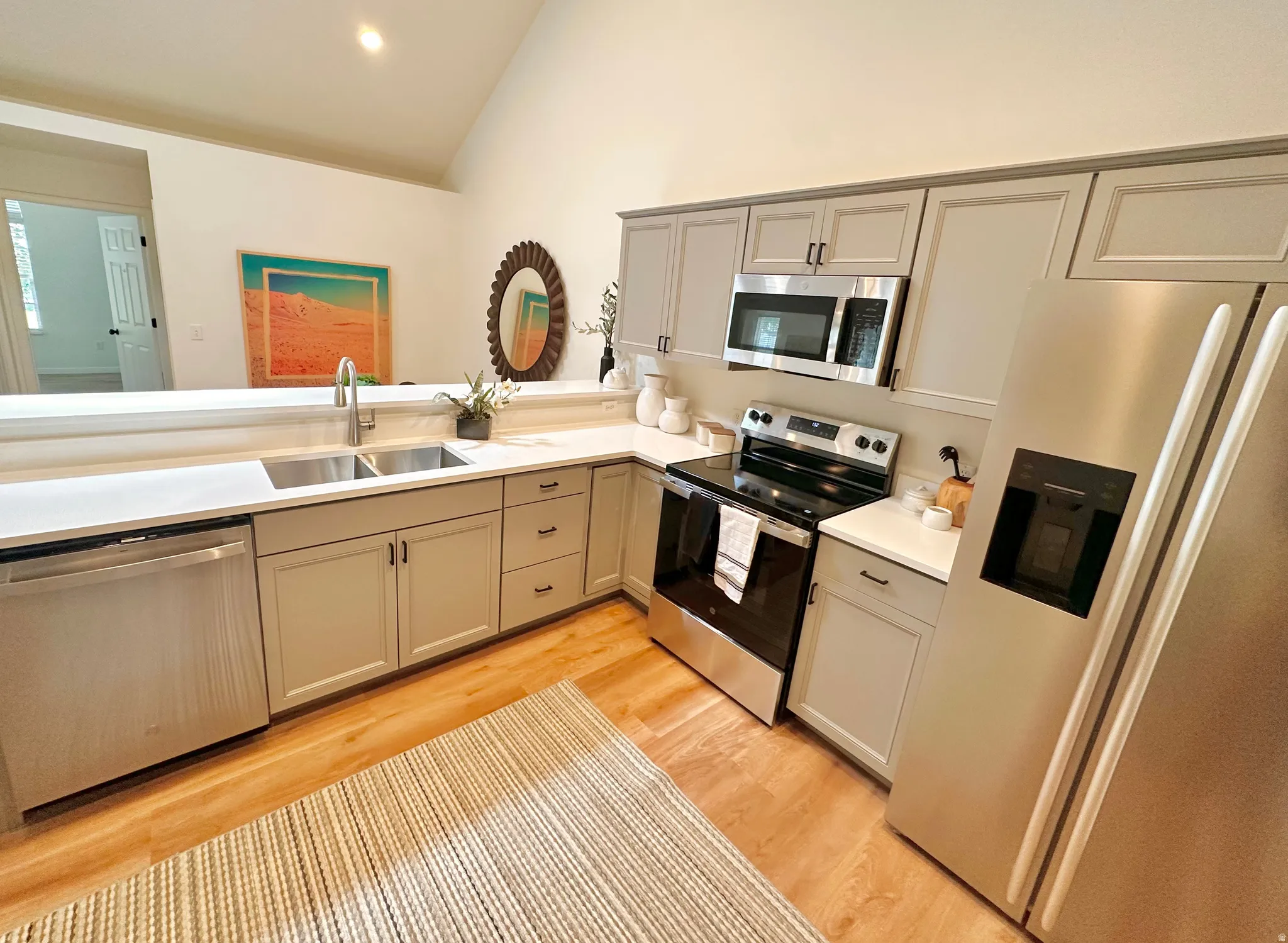 Kitchen featuring light wood-finish flooring, white countertops, light gray cabinetry, and stainless steel appliances including a refrigerator, range, microwave, and dishwasher