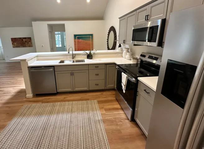 Modern kitchen featuring light wood-finish flooring, white countertops, gray cabinetry, and stainless steel appliances including a refrigerator, range, microwave, and dishwasher