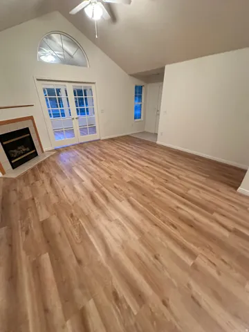 Vaulted ceilings with a ceiling fan, wood-finish flooring, and a fireplace with a tile surround
