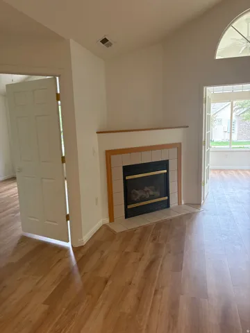 Wood-finish flooring throughout, featuring a corner fireplace with a tiled hearth and wood mantel