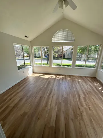 Spacious room featuring vaulted ceilings, a ceiling fan, and extensive wood-finish flooring