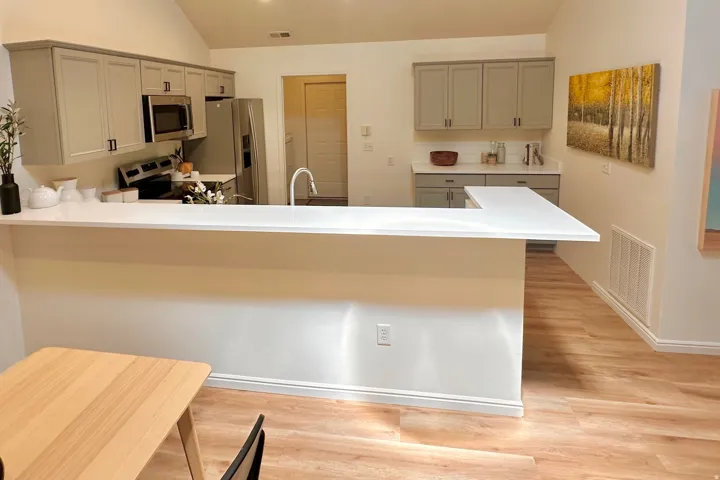 Kitchen featuring a peninsula breakfast bar, wood-finish flooring, vaulted ceilings, grey shaker-style cabinetry, and stainless steel appliances
