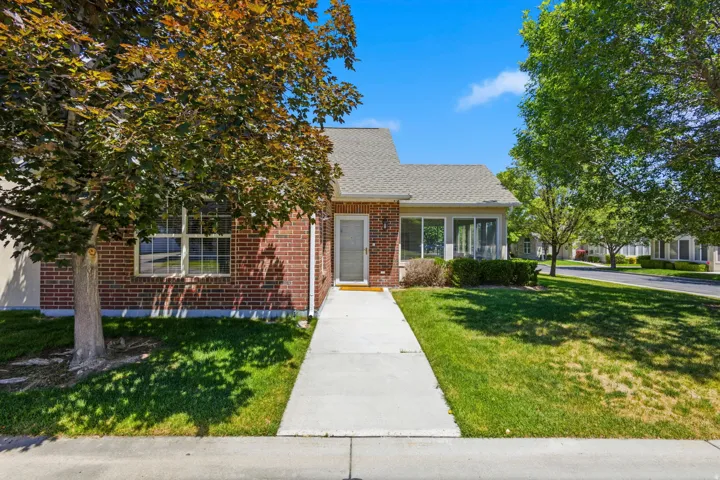 Brick exterior with a gabled roofline, featuring a concrete walkway, mature trees, and established landscaping