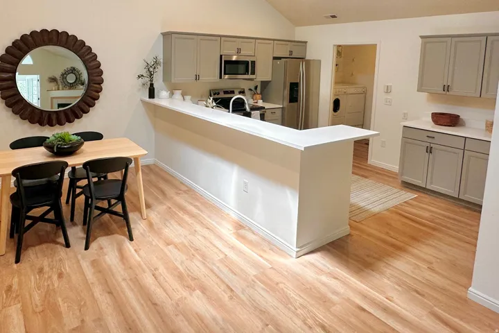 Open-concept kitchen featuring wood-finish flooring, light gray cabinetry, stainless steel appliances, and a breakfast bar with white countertops