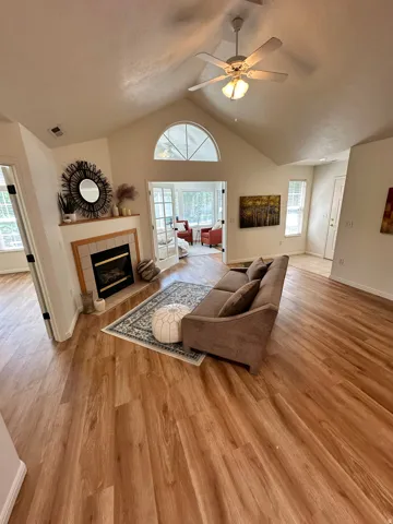 Bright living area featuring wood-finish flooring, a vaulted ceiling, and a fireplace with a tile surround and wood mantel