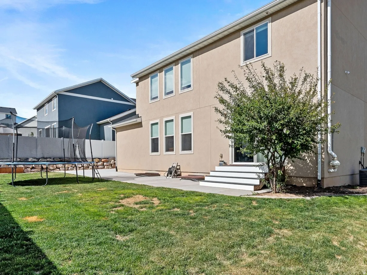 Expansive backyard featuring a stucco exterior, concrete patio, white privacy fencing, and a decorative rock border