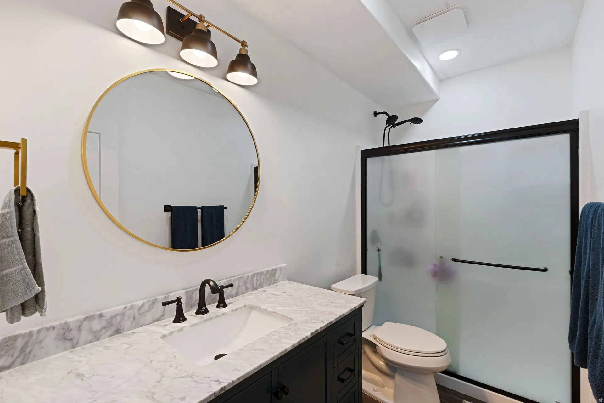 Basement bathroom featuring a dark vanity with a white countertop, an undermount sink, and a circular gold-framed mirror