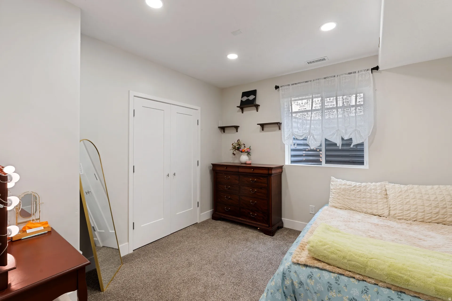 Basement bedroom with recessed lighting illuminates a carpeted room featuring a double-door closet with contemporary hardware