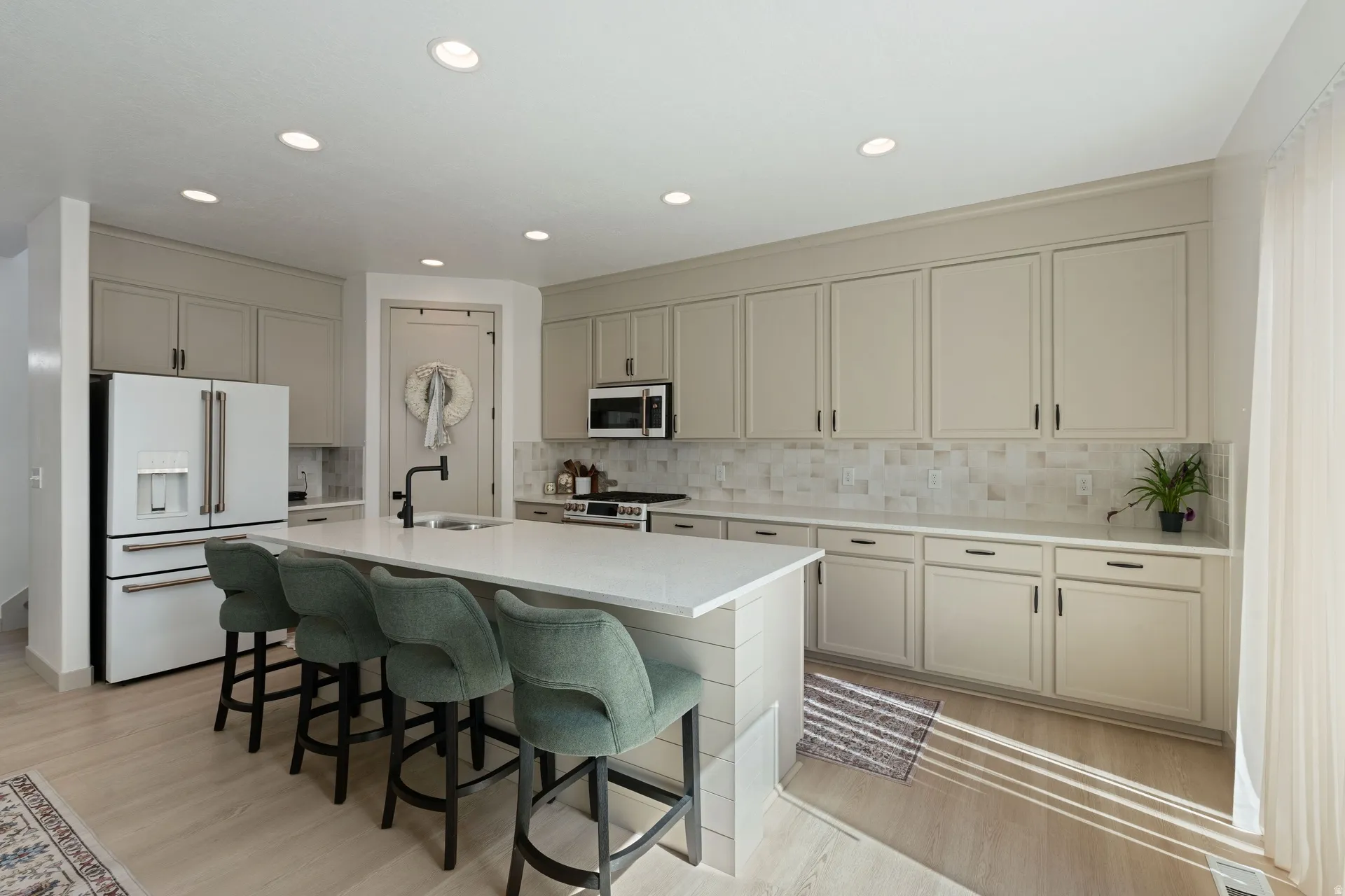 Open-concept kitchen featuring light-toned cabinetry with matte black hardware, a white countertop island with shiplap detailing, recessed lighting, wood-finish flooring, and a patterned tile backsplash