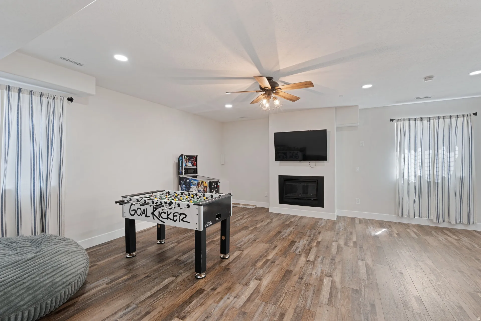 Basement spacious entertainment area featuring wood-finish flooring, a built-in fireplace, a ceiling fan with integrated lighting, and recessed ceiling lights