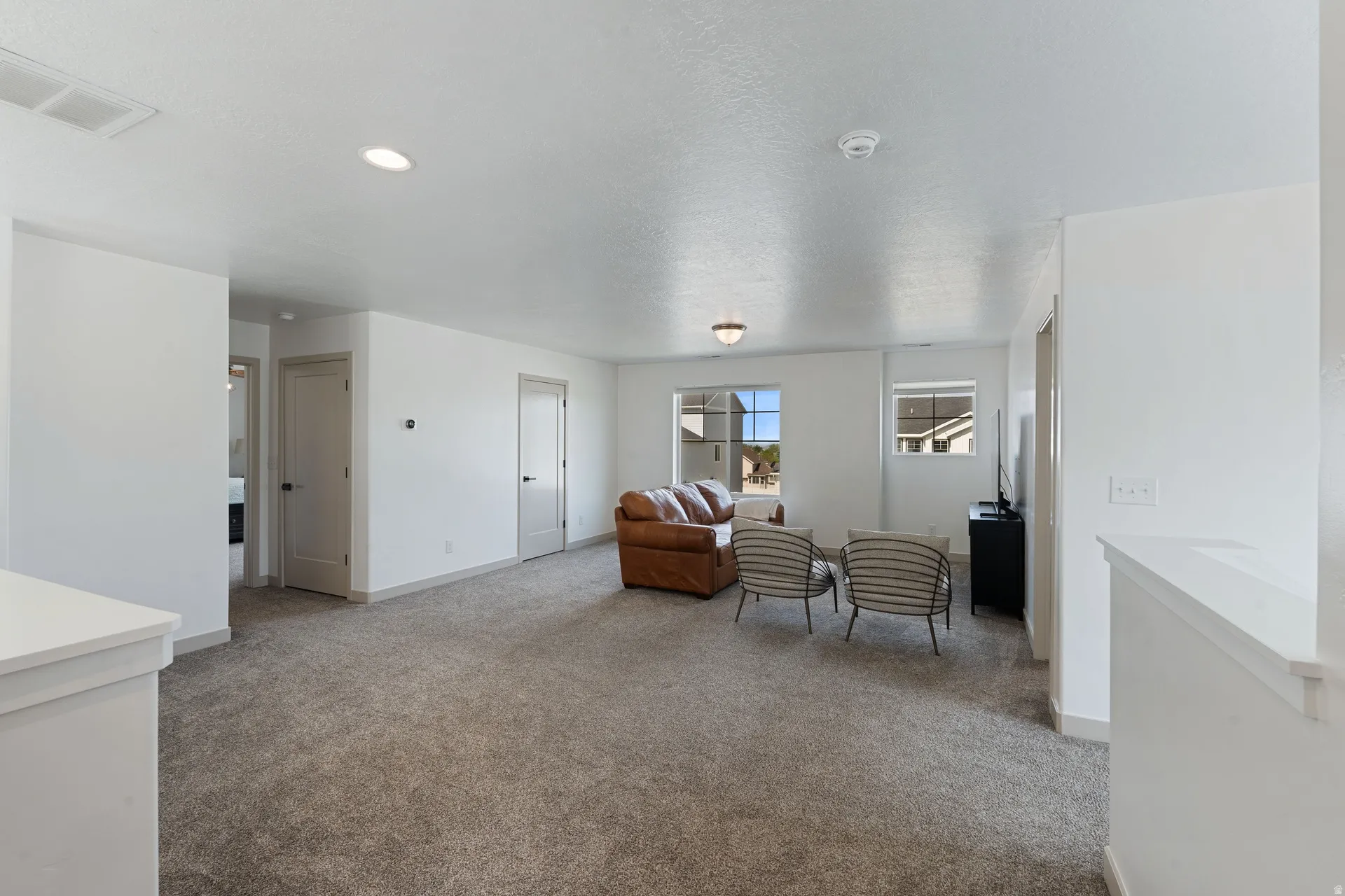 Carpeted common area featuring bright white walls, multiple windows, recessed lighting, and a built-in railing