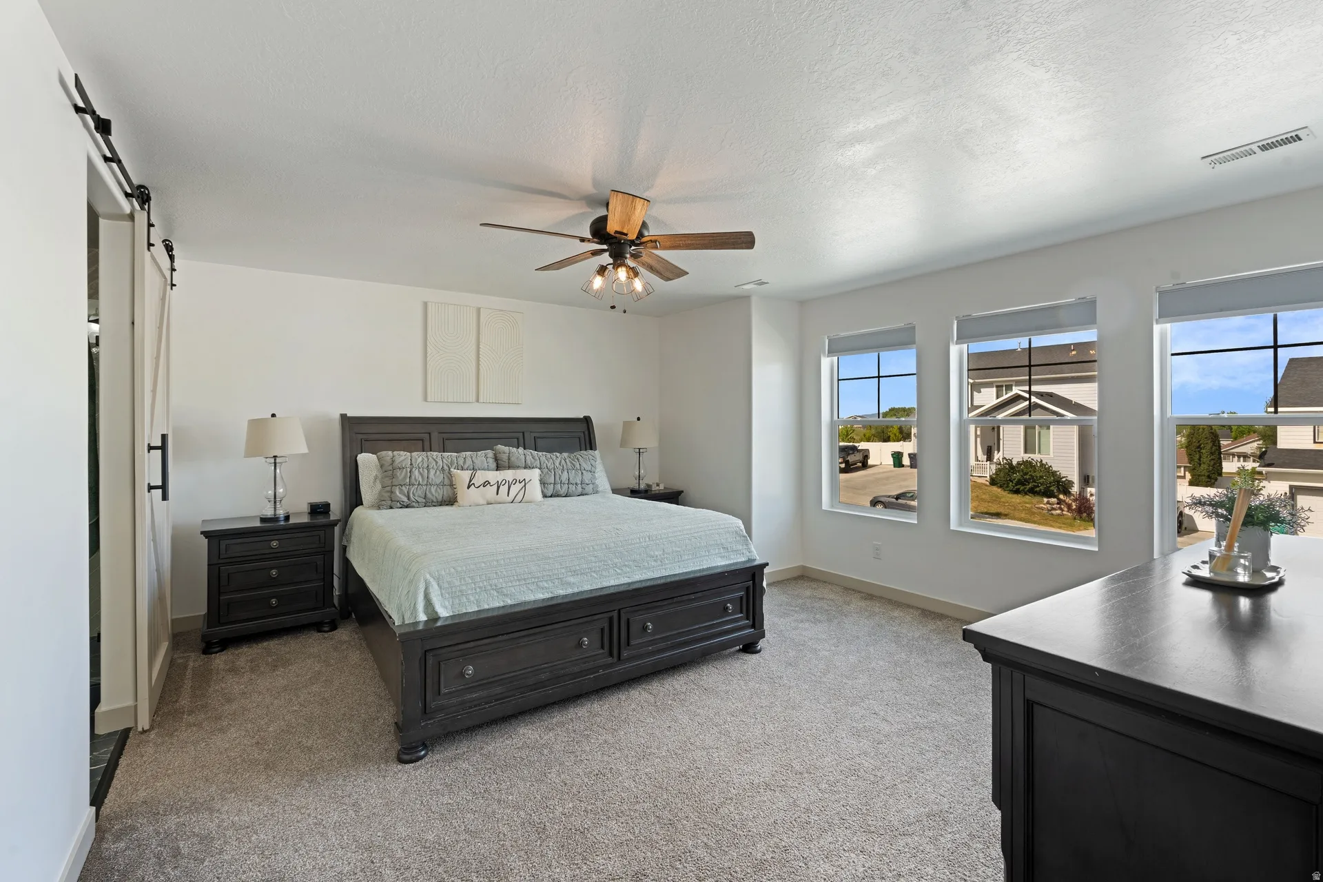 Primary bedroom featuring a ceiling fan with integrated lighting, three large windows, and a white barn door