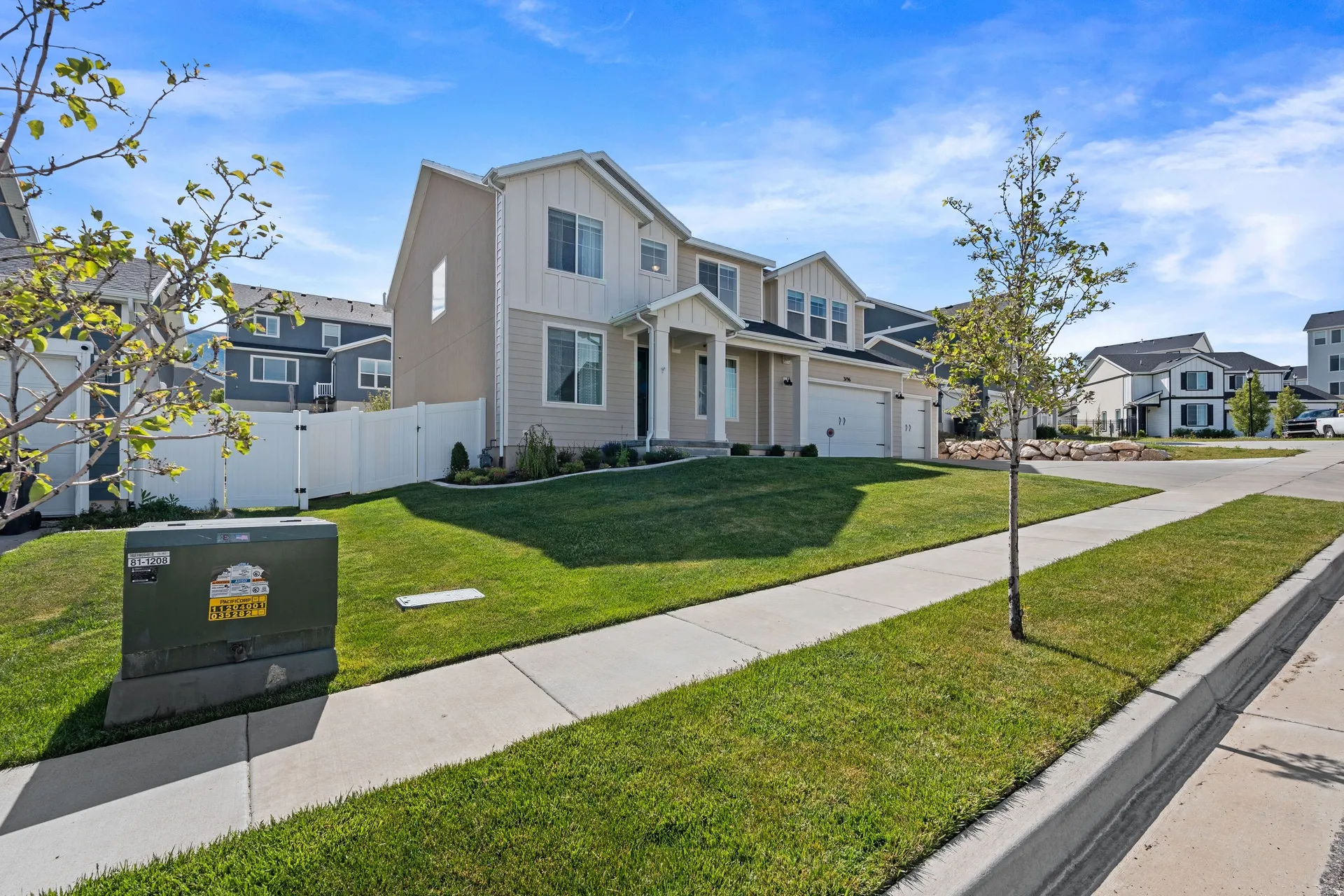 Two-story residence featuring light-colored siding with vertical accents, an attached two-car garage, a covered front porch, and a well-maintained front lawn with a sidewalk