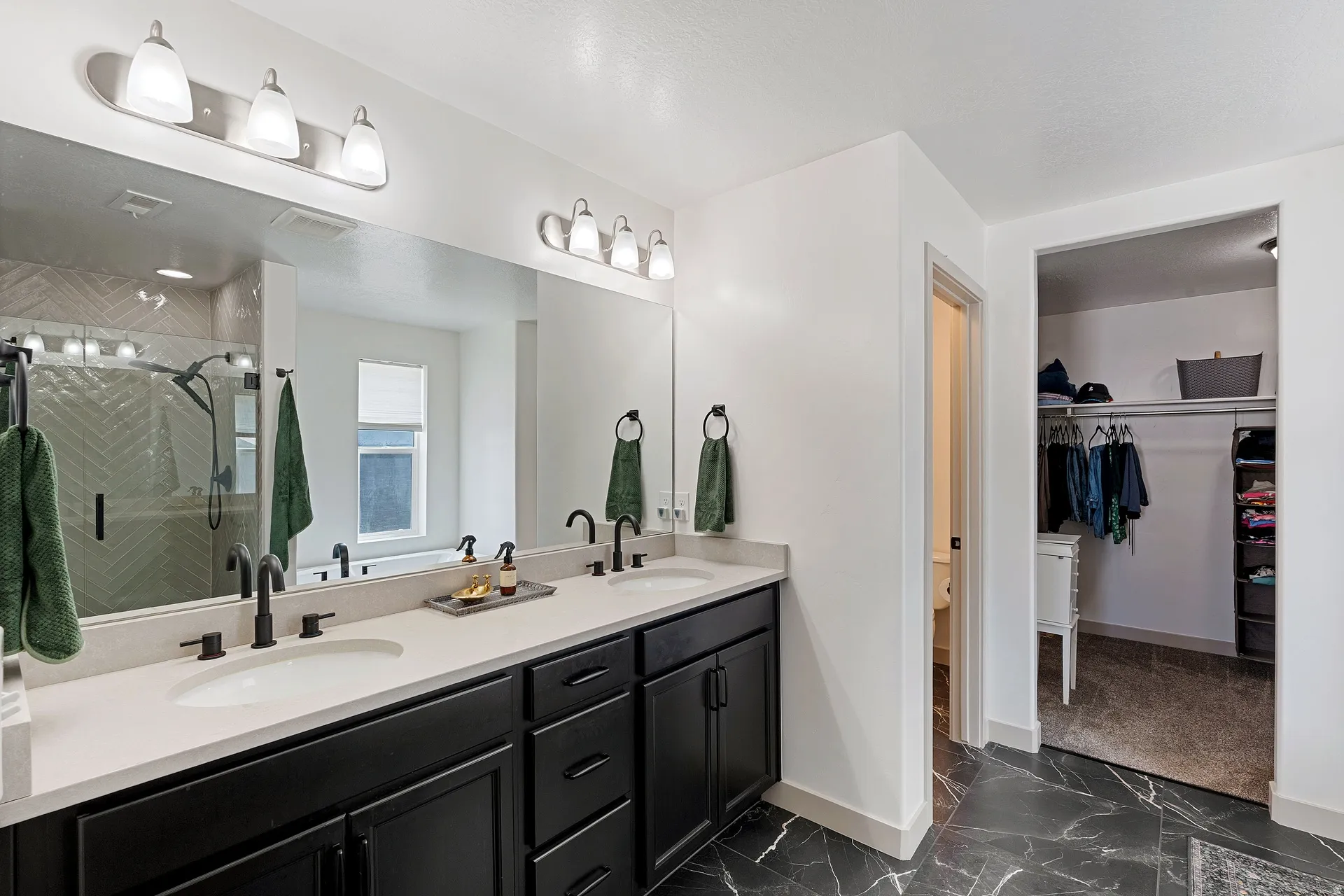 Primary bathroom featuring a dual vanity with matte black hardware, stone-finish countertops, black cabinetry, and a large mirror