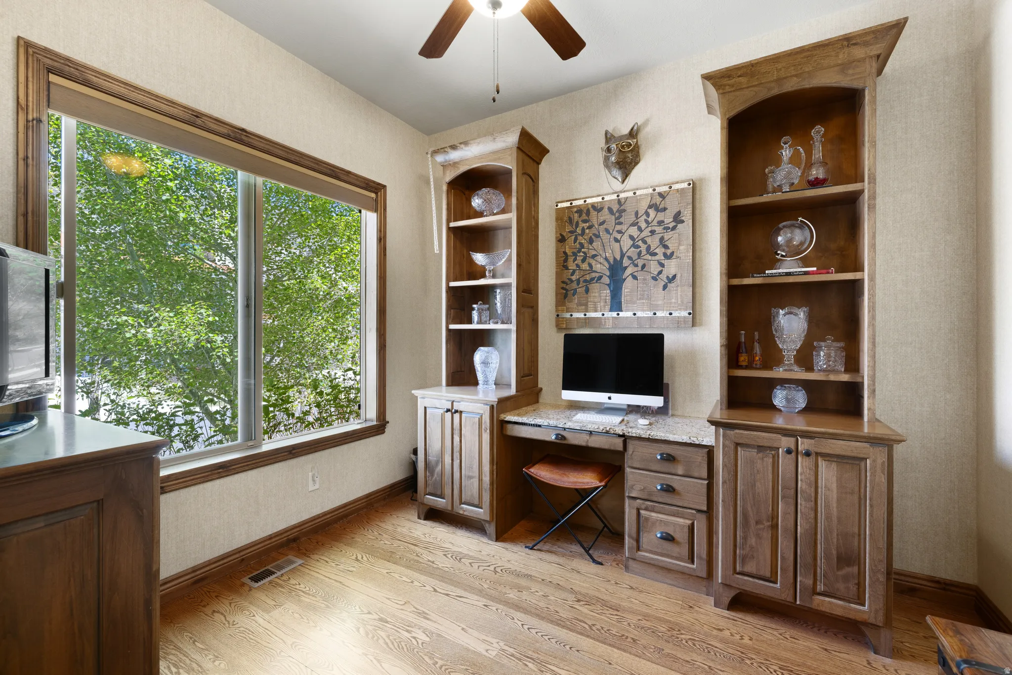 Room featuring built-in wood cabinetry with stone countertops, a large window with wood trim, wood-finish flooring, and a ceiling fan