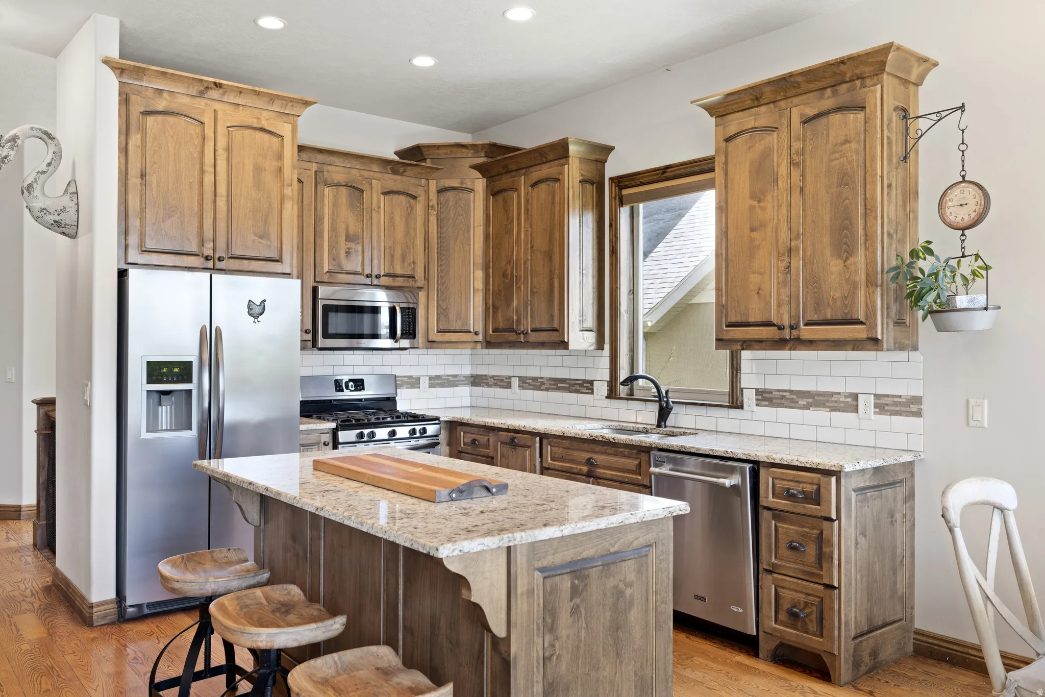 Kitchen featuring wood-finish cabinetry, stainless steel appliances, a center island with light-toned countertops, and a white subway tile backsplash with decorative accents