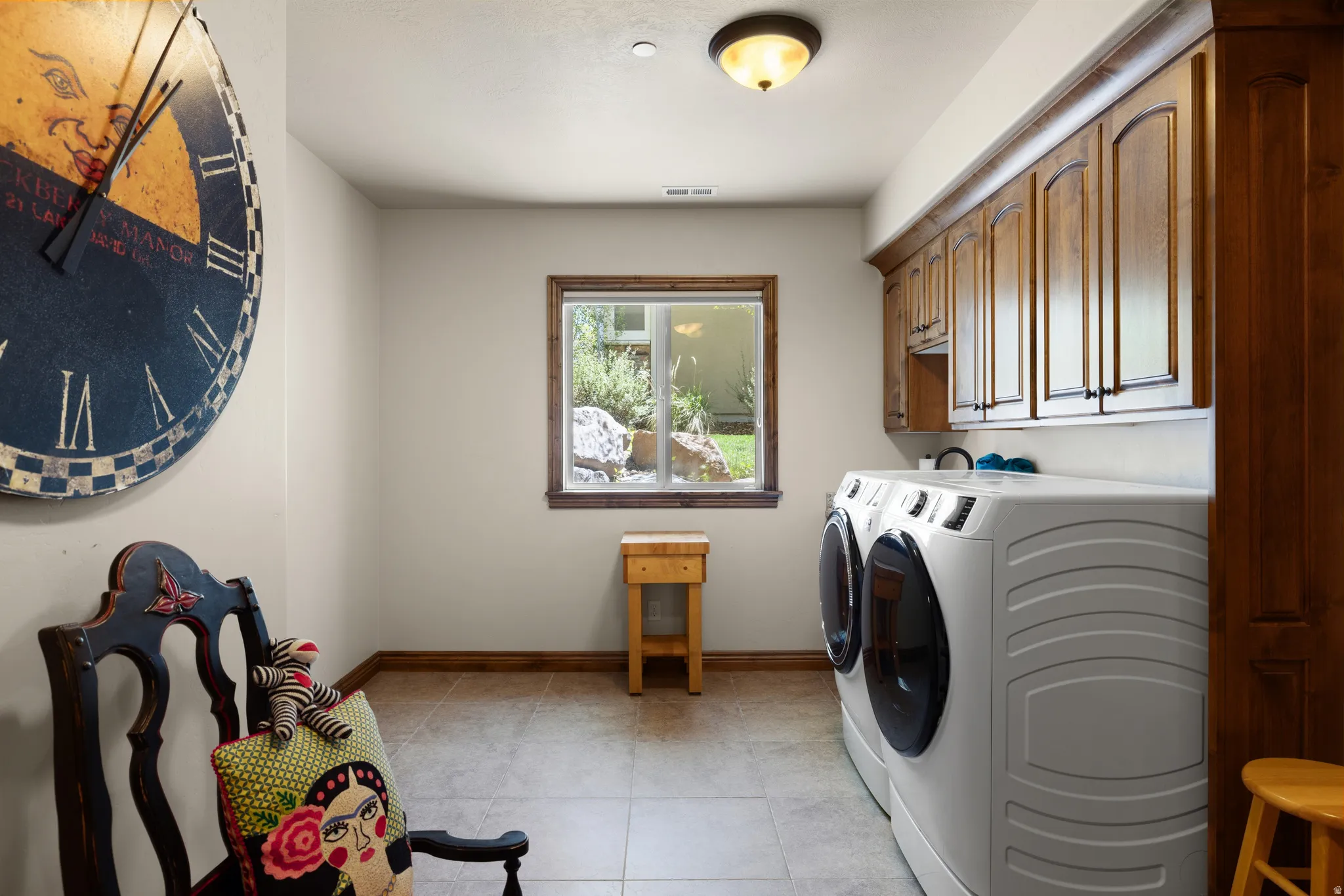 Laundry area featuring light-toned walls, tile flooring, and wood-finish cabinetry