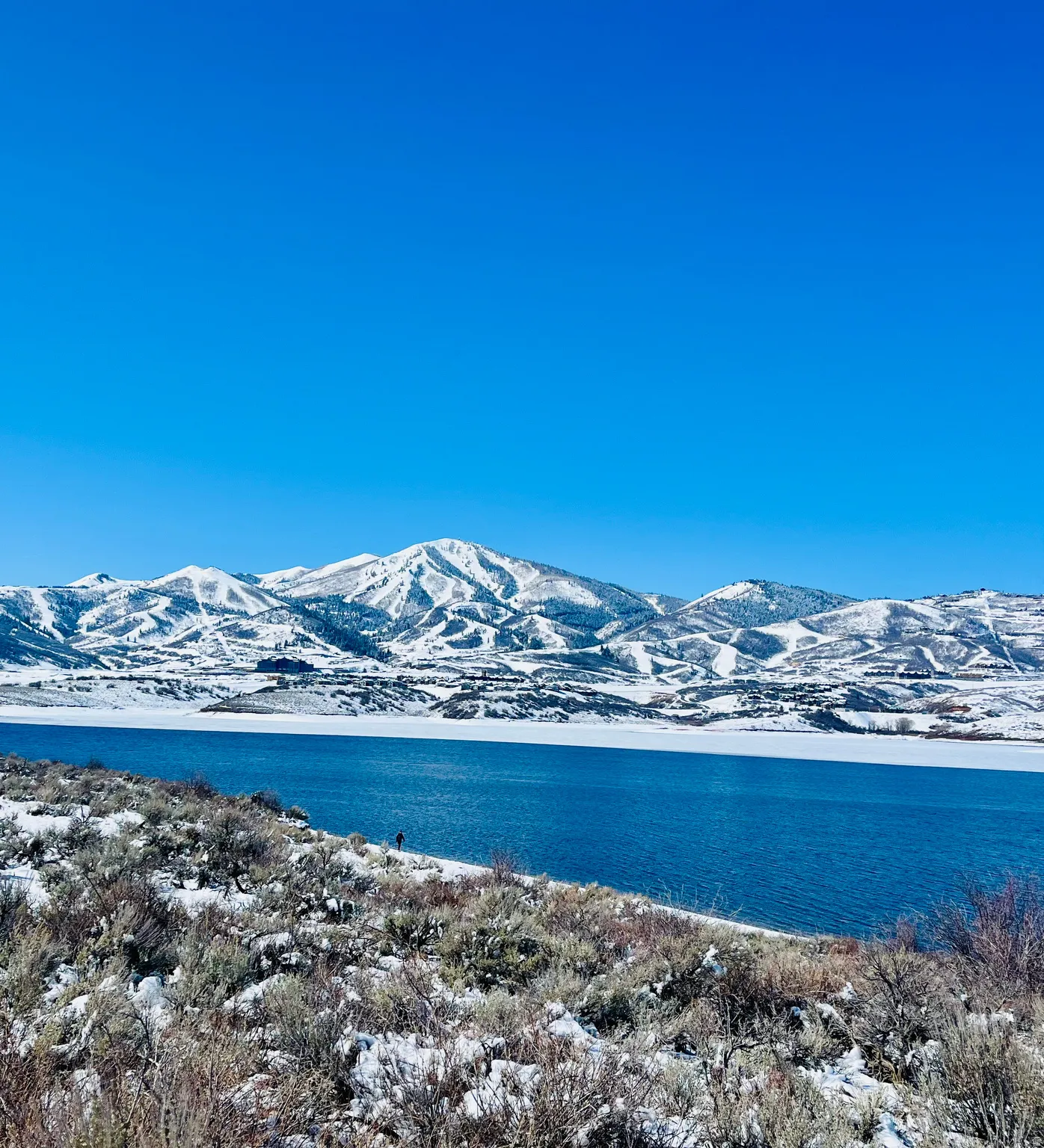 Expansive water body with snow-covered mountains in the background, featuring distinct ski trails