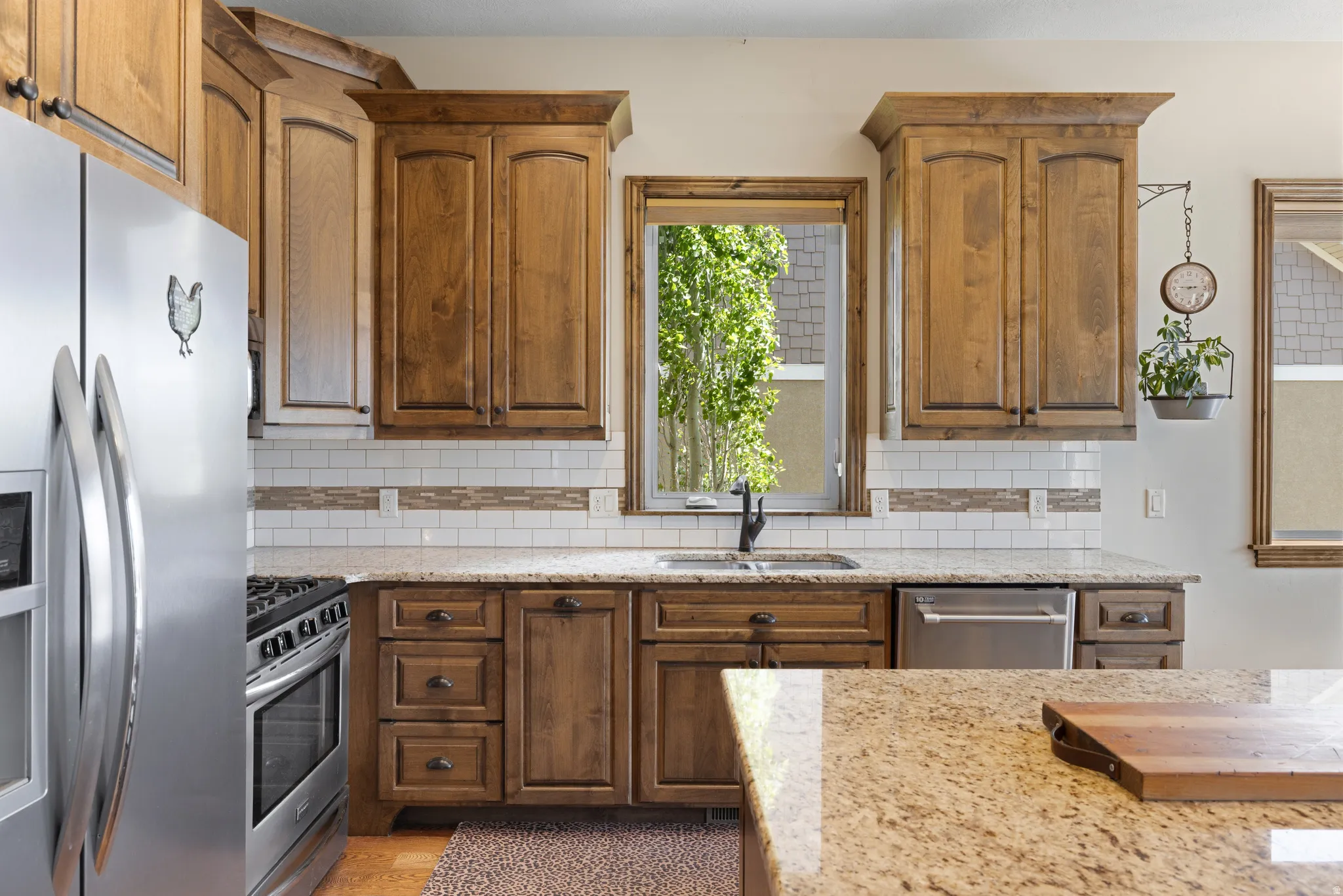 Kitchen featuring wood cabinetry with dark hardware, granite countertops, subway tile backsplash, and stainless steel appliances