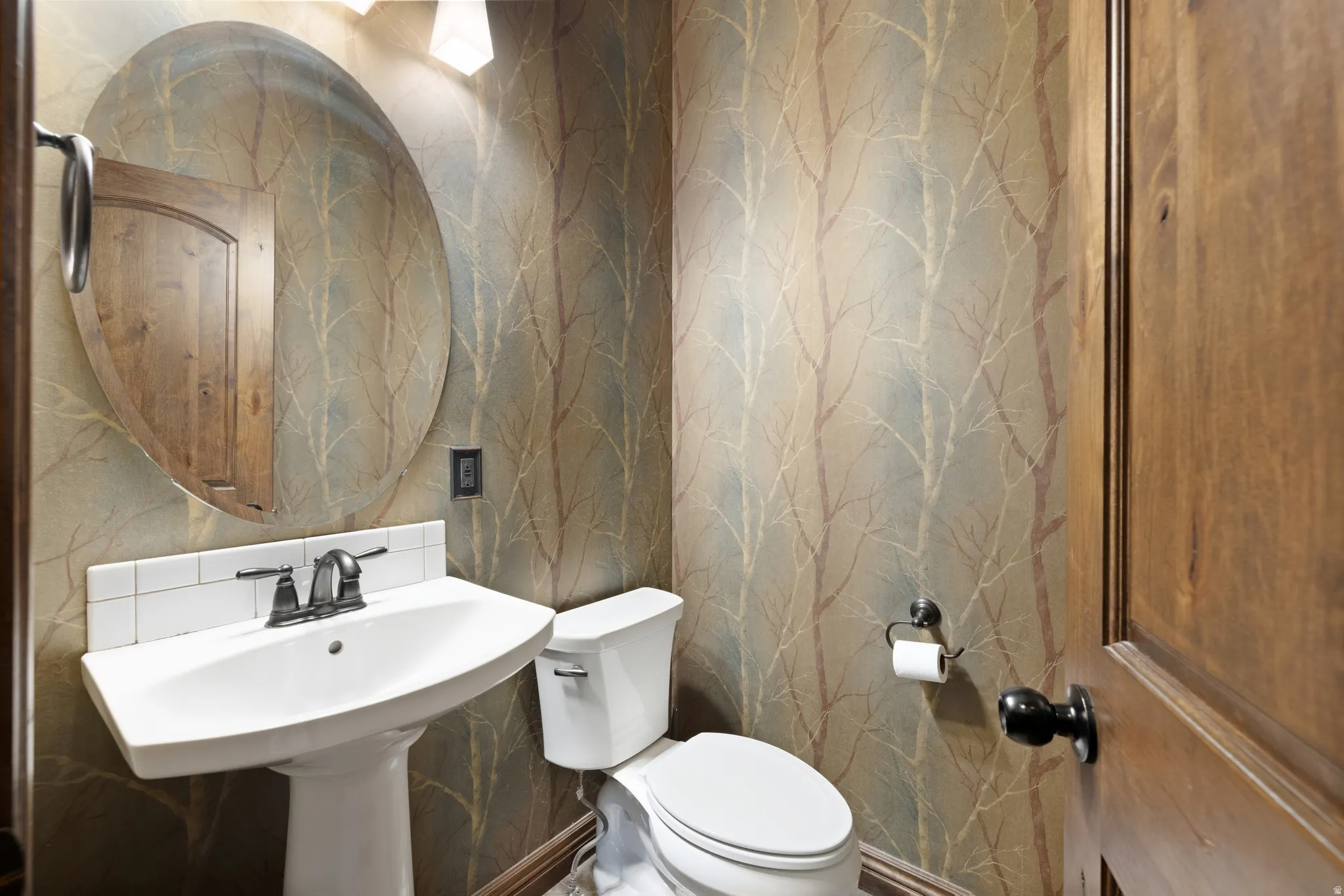 Pedestal sink with an oval mirror, accented by a subtle patterned wallpaper