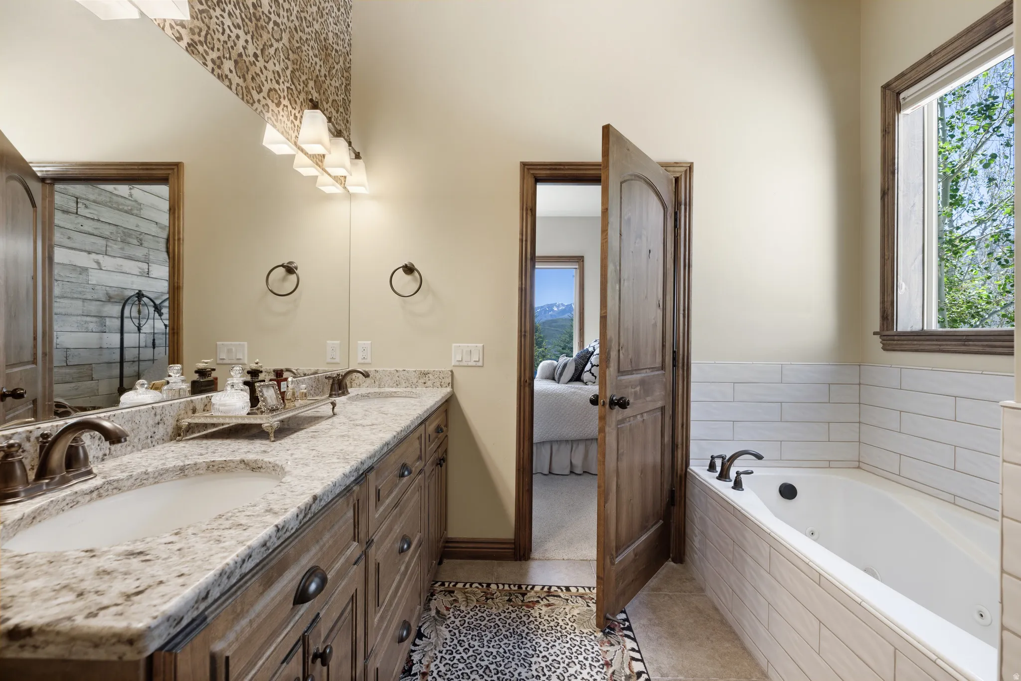 Bathroom featuring a dual vanity with granite-style countertops and undermount sinks, a built-in tub with tile surround, a large window, and a wooden interior door